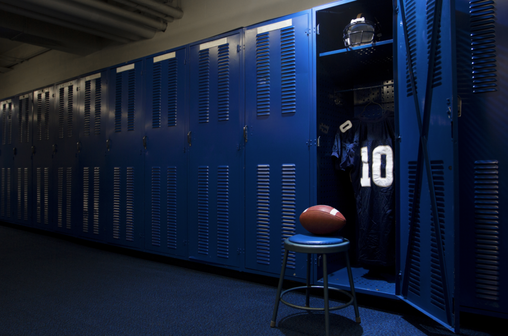 Youth sports costs are increasing. Equipment and fees for football can be especially steep. Image of football equipment in a locker room.