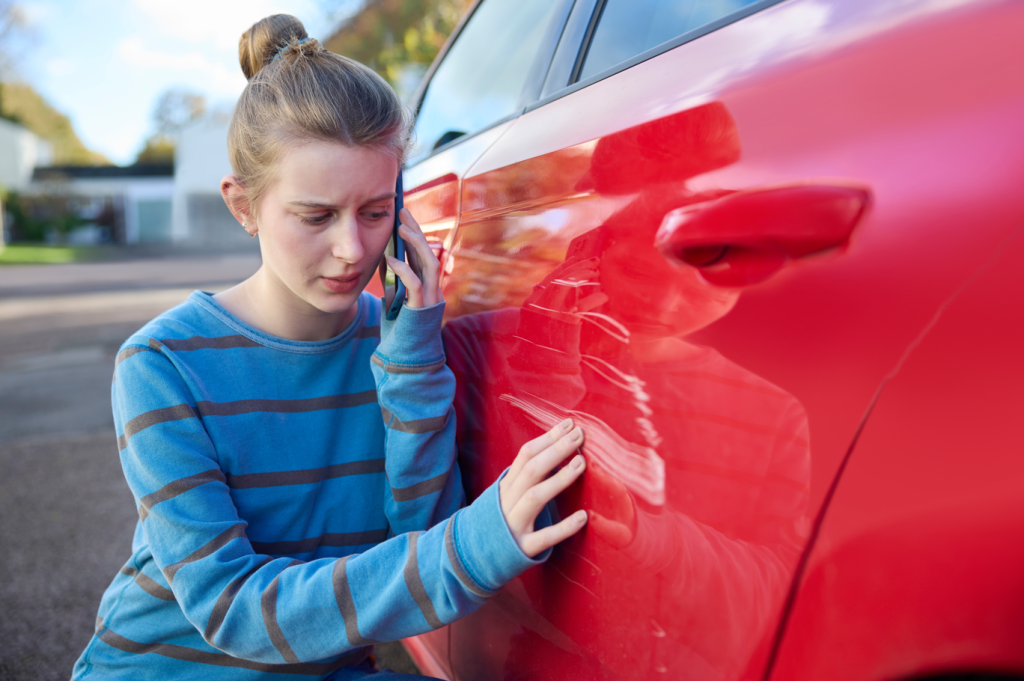 Teenager looking at the side of her new car which has been scratched up during a collision. She's concerned about teens and budgeting and how this will affect her savings.